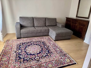 Una sala de estar con un sofá seccional gris, un tapete estampado y un mueble de madera.