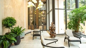 A modern lobby with seating, a wooden sculpture, and a large window with a view of greenery. - The Lumi Apartments by XOI Residences (Hanoi)