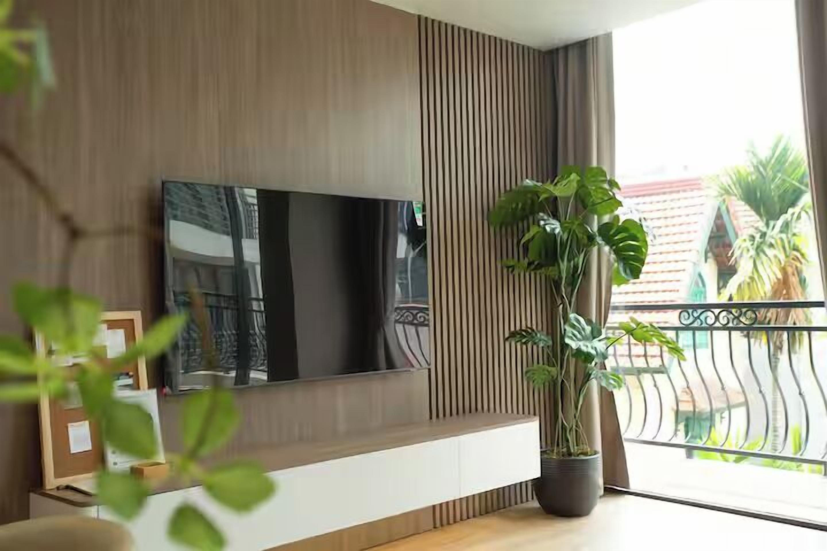 Un salon moderne avec un téléviseur à écran plat fixé à un mur en bois, une plante en pot et un balcon doté d’une balustrade.