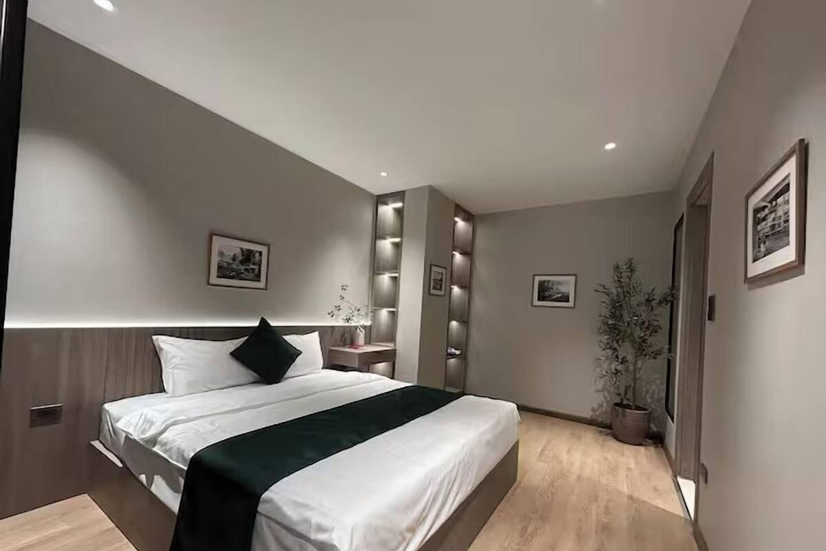A modern bedroom with a large bed, bedside tables, a mirror, and wall-mounted lighting.