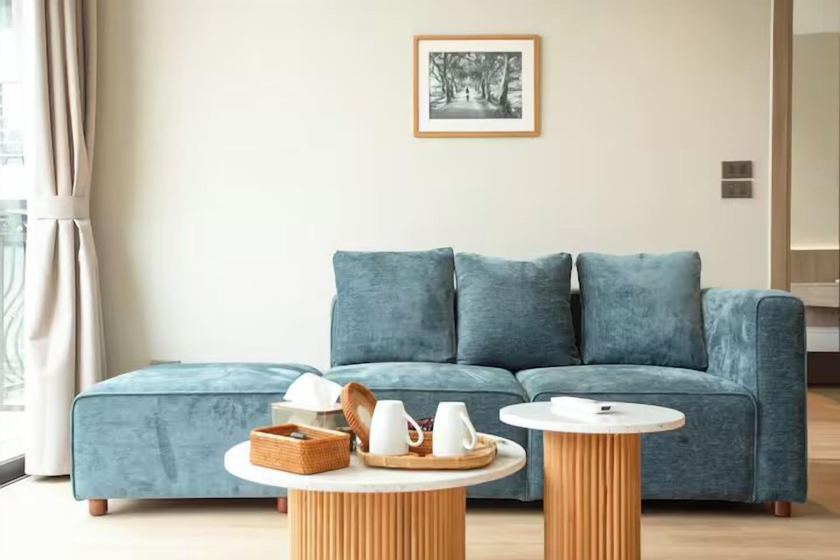 Una sala de estar moderna con un sofá azul verdoso, dos mesas redondas de madera y un cuadro en la pared.