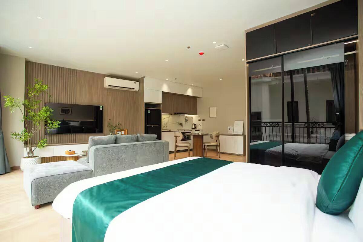 A modern hotel room with a large bed, a sofa, a dining area, and a balcony with a view.