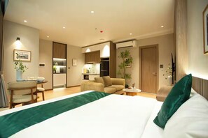Ein modernes Hotelzimmer mit einem großen Bett, einer Couch, einem kleinen Tisch und einer Küchenzeile im Hintergrund.