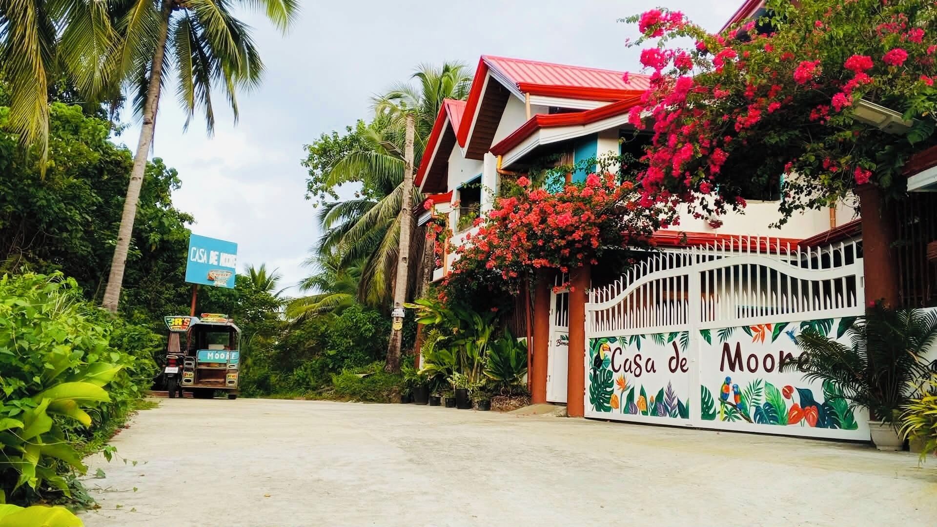 A tropical resort with a colorful entrance gate, lush greenery, and a clear sky.