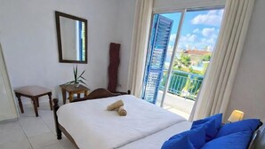 Hotelkamer met een bed, nachtkastje met lamp, stoel, klein tafeltje met plant en raam met uitzicht.