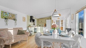 Ett modernt kök med vita skåp, en matplats med ett vitt bord och stolar samt ett mysigt vardagsrum med en soffa.