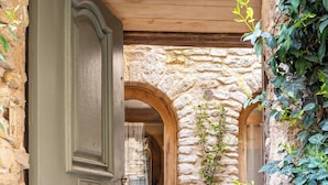 A rustic stone-walled courtyard with a wooden door, a bench, and a table. - L’Unique – Voûte du XVIIIe & Élégance Incomparable (Goult)