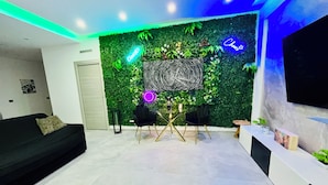 A modern living room with a green wall, a black sofa, a dining table with chairs, and a TV mounted on the wall. - Milan Bicocca Apartment, cozy luxury apartment, comfortable particular (Cinisello Balsamo)