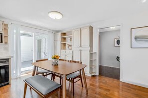 A dining area with a wooden table and chairs, a vase with flowers, and white cabinetry.