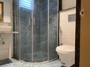 A bathroom with a glass-enclosed shower, a white sink, and a toilet. - Rohm Staycations (Gopalpur)