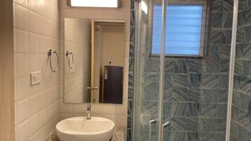 Un baño con un lavabo blanco, un espejo y una ducha con puerta de cristal.