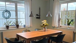 En matplats med ett träbord och svarta stolar, en vas med blommor och utsikt genom stora fönster.