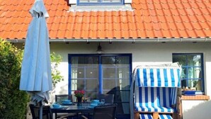 Ett hus med ett rött tegeltak, en täckt uteplats med ett bord och stolar samt en randig utomhusstol.