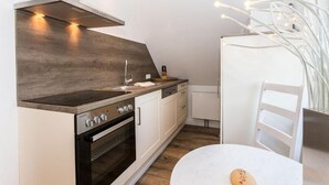 A compact kitchen with a stove, oven, and white cabinets. - Seerose Sylt - Modern 3-room apartment with dune view and balcony (Sylt)