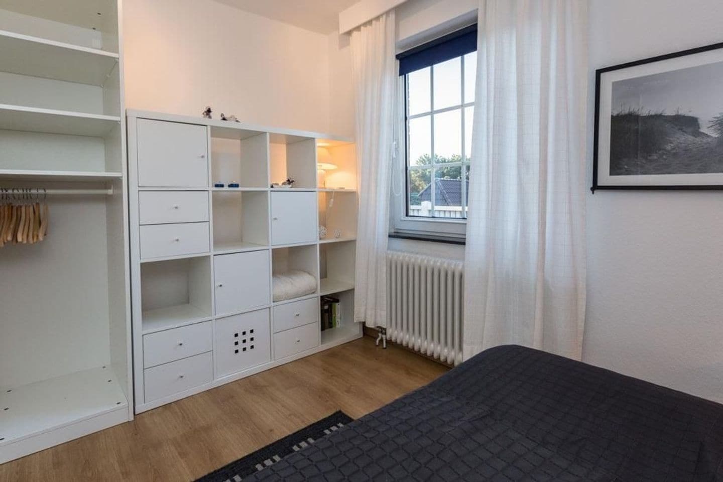Un dormitorio con cama, armario, radiador y ventana con cortinas.