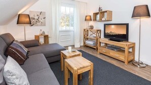 A modern living room with a grey sofa, wooden coffee table, and TV stand. - Seerose Sylt - Modern 3-room apartment with dune view and balcony (Sylt)