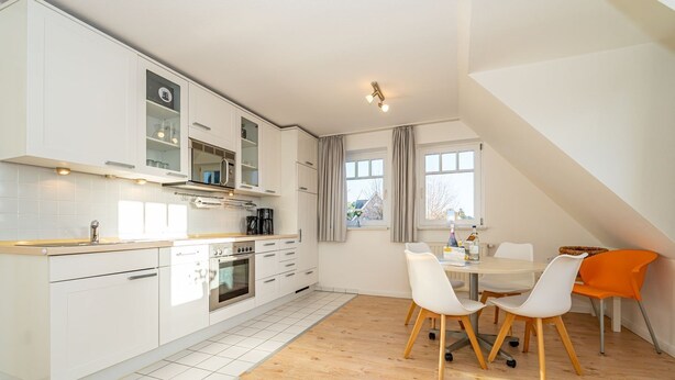 A modern kitchen with white cabinets, a built-in oven, and a dining area with a table and chairs. - Conwind apartment 5b - New with us! Apartment with terrace and private parking space (Sylt-Ost)