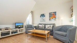 A modern living room with a flat-screen TV, grey sofas, a wooden coffee table, and artwork on the walls. - Conwind apartment 5b - New with us! Apartment with terrace and private parking space (Sylt-Ost)