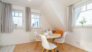 A dining area with a round table, four chairs, and a view of the city through large windows. - Conwind apartment 5b - New with us! Apartment with terrace and private parking space (Sylt-Ost)