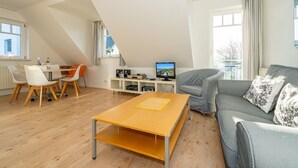 A modern living room with a wooden coffee table, grey sofa, and white chairs. - Conwind apartment 5b - New with us! Apartment with terrace and private parking space (Sylt-Ost)