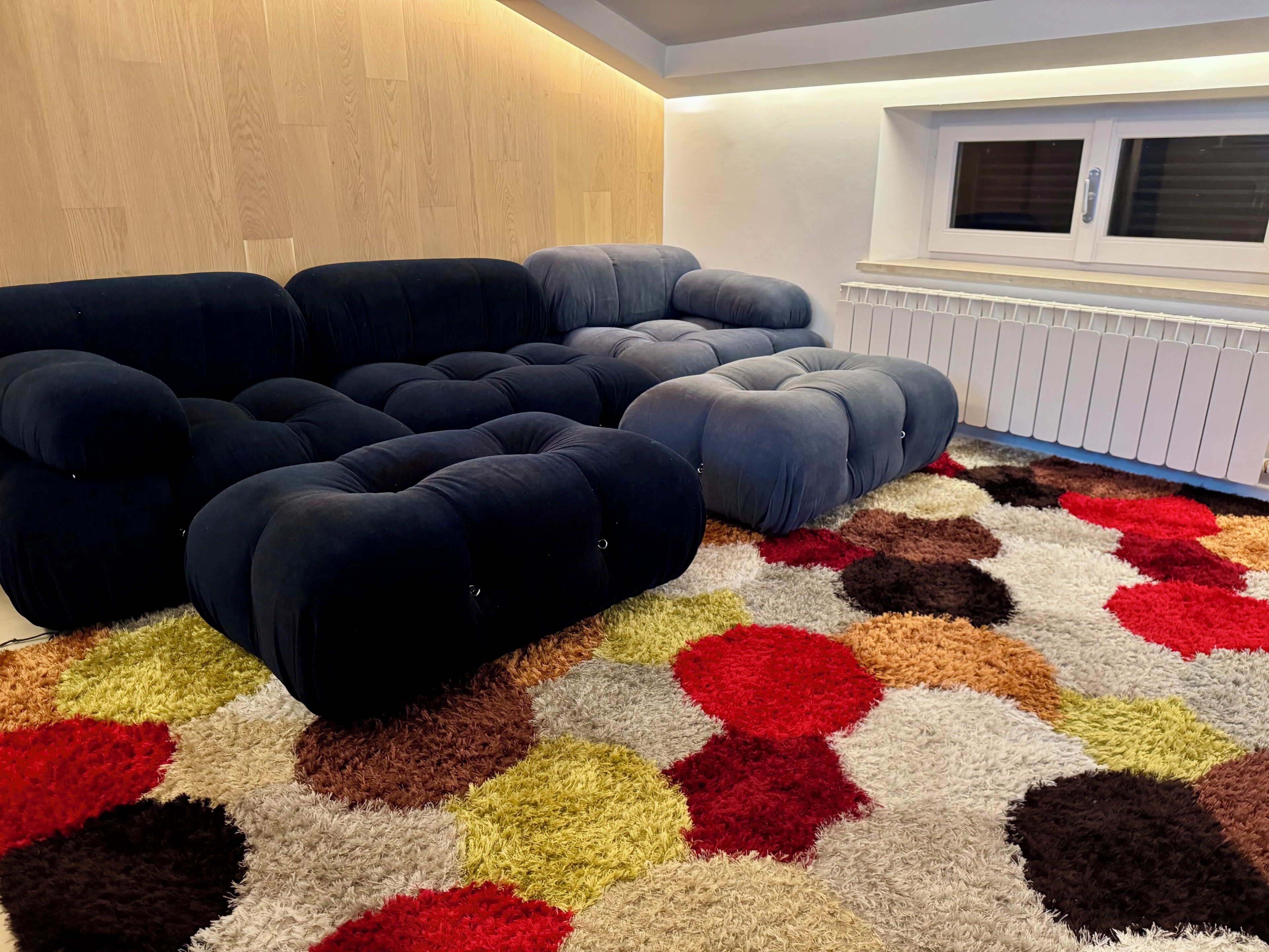 A room with a sectional sofa, a patterned rug, and a radiator.