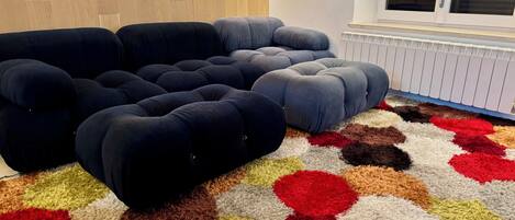 A room with a sectional sofa, a patterned rug, and a radiator.