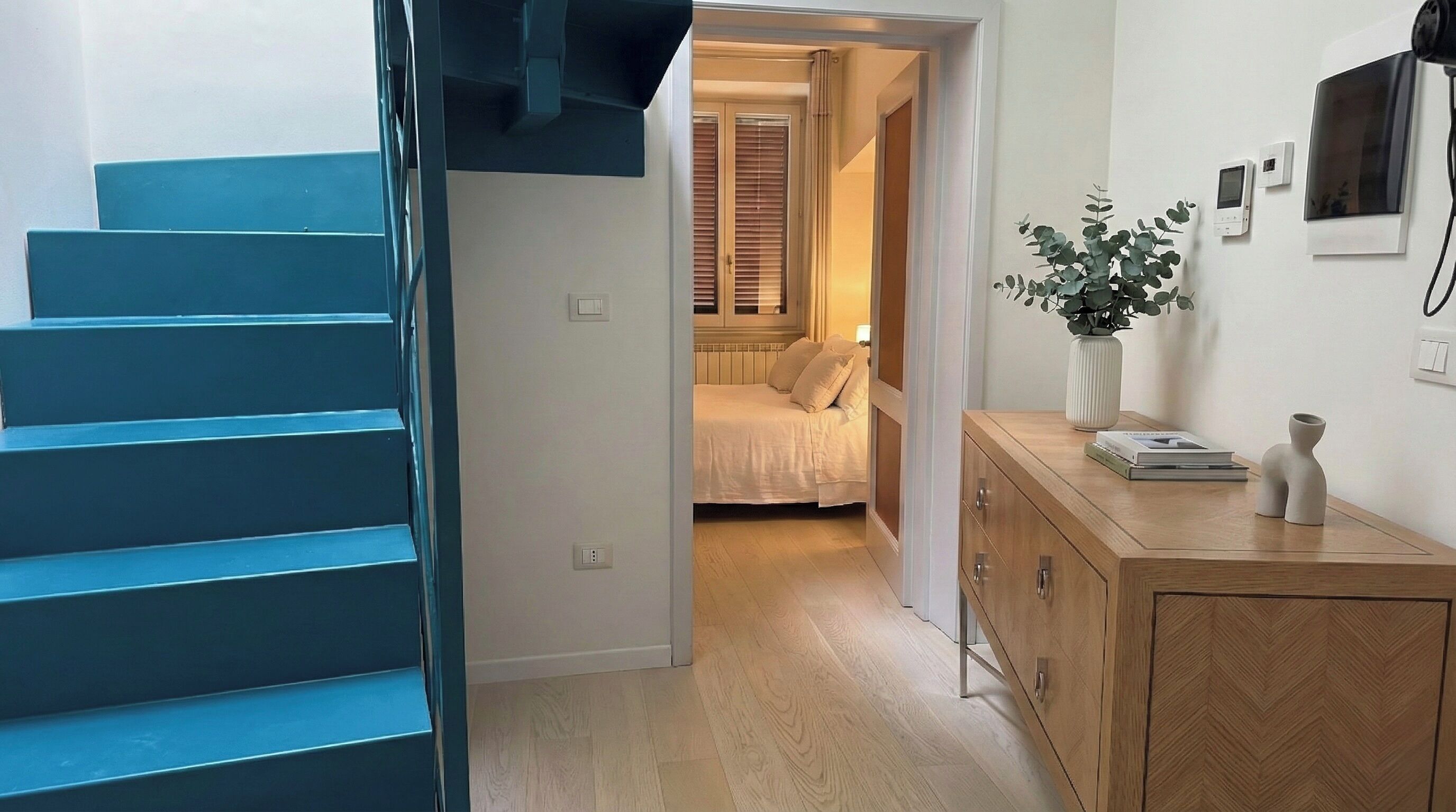 A staircase leading to a bedroom with a bed, a bedside table, and a wall-mounted TV.