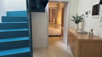 A staircase leading to a bedroom with a bed, a bedside table, and a wall-mounted TV.