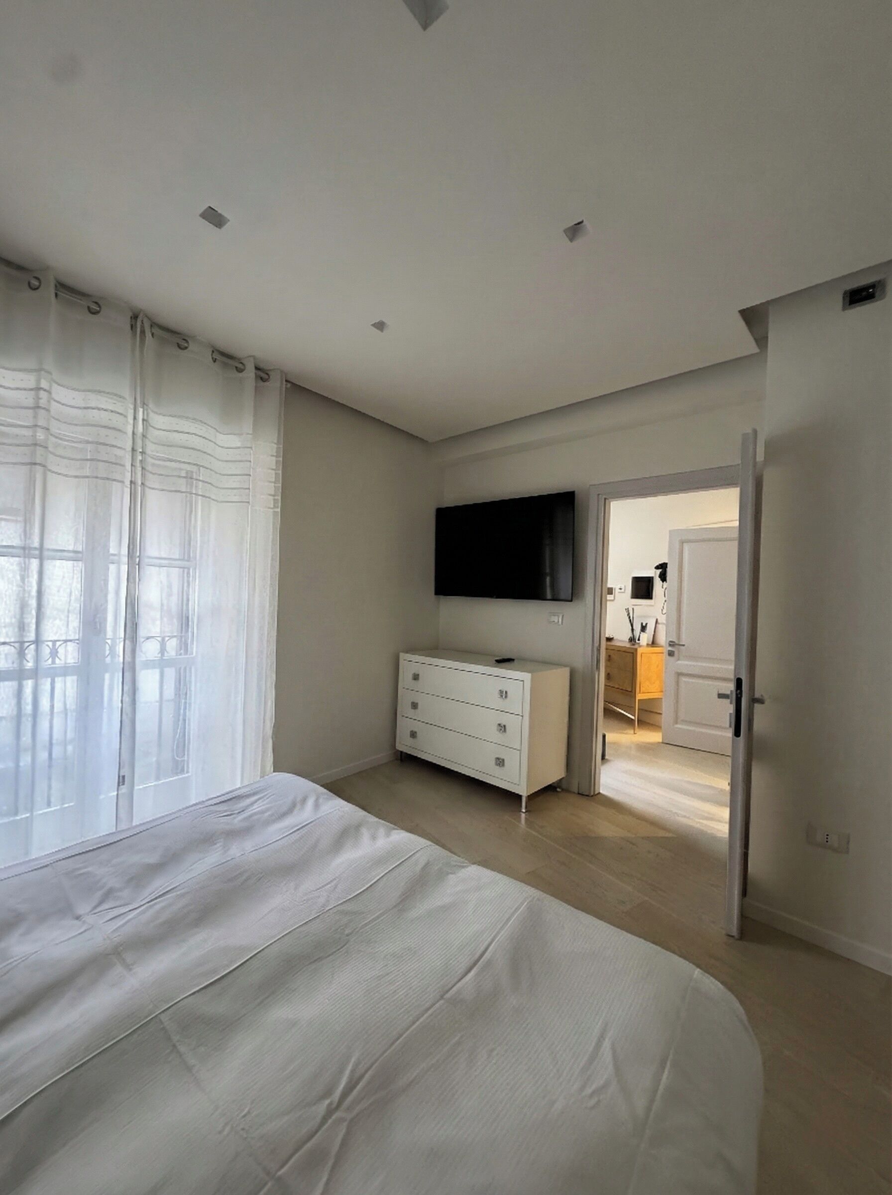 Un dormitorio con cama, cómoda, televisor y puerta que da a otra habitación.