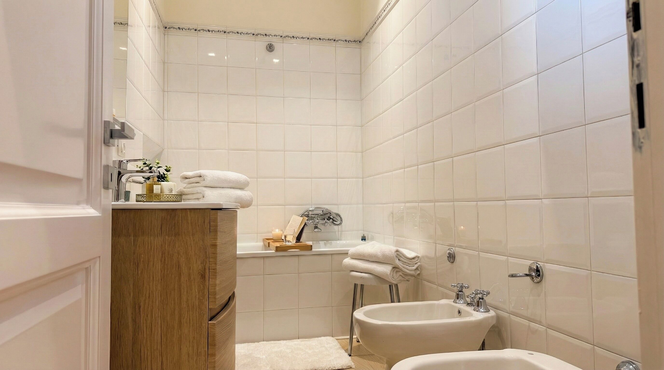 A modern bathroom with white tiles, a wooden vanity, a sink, and a bathtub.