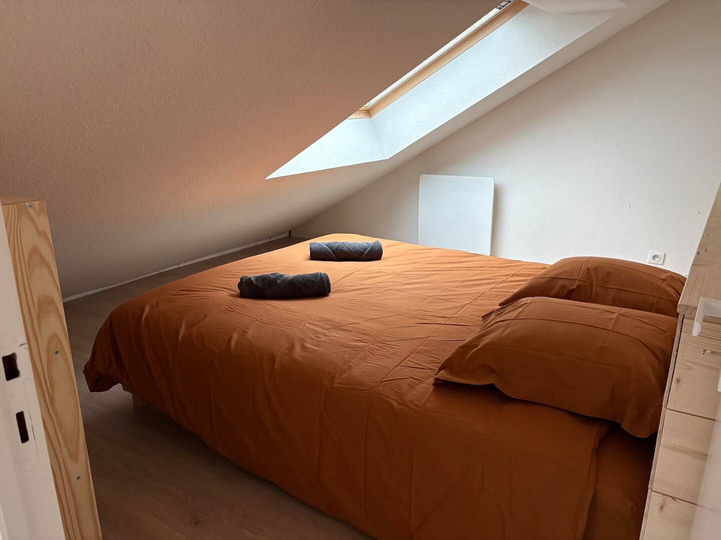 Quarto com teto inclinado, cama com roupa de cama laranja e um claraboia.