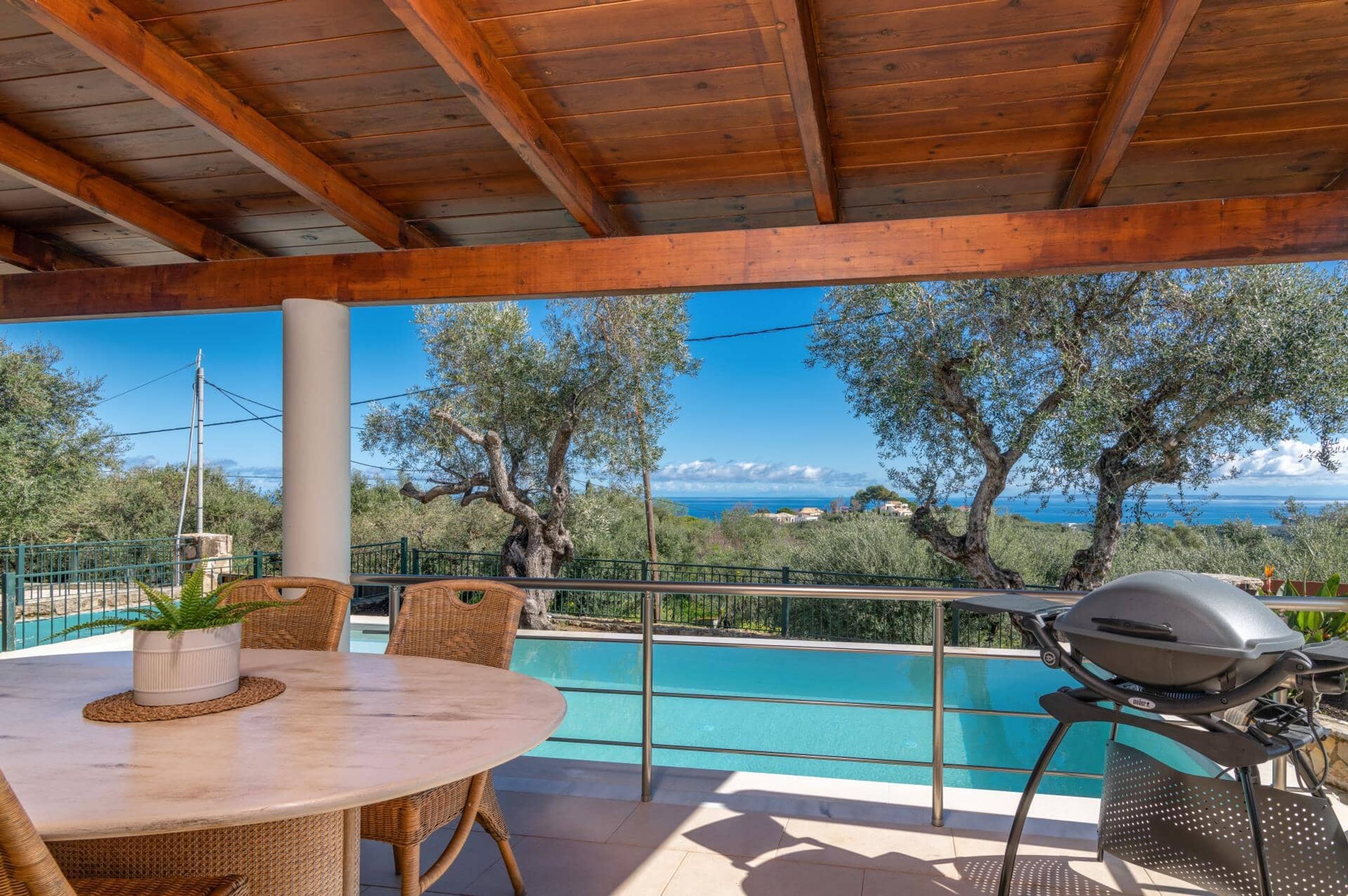 A covered outdoor area with a pool, wooden ceiling, and a view of the sea.