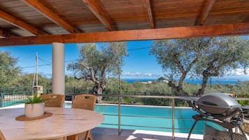 A covered outdoor area with a pool, wooden ceiling, and a view of the sea.