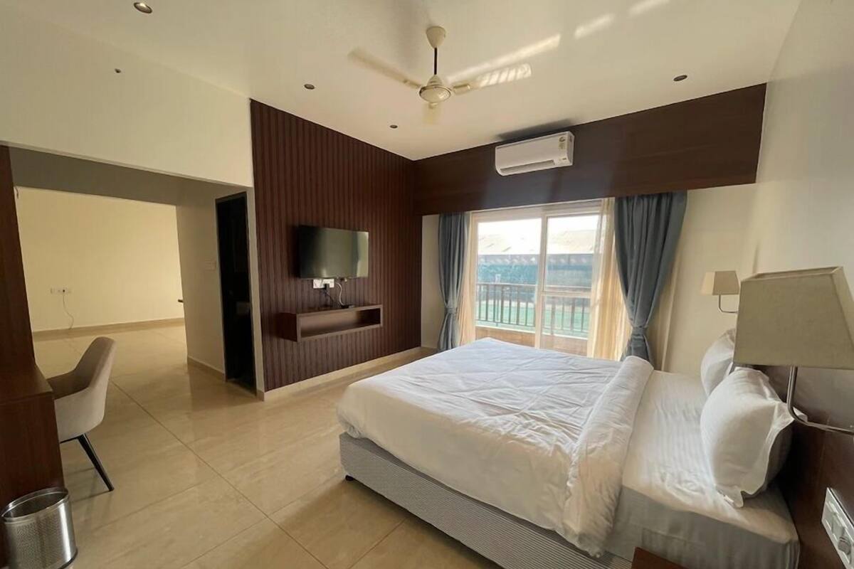 A modern hotel room with a large bed, a television, a ceiling fan, and a window with curtains.