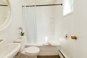 A bathroom with a toilet, sink, shower curtain, and a towel on the floor. - Gateway Suites: Pet-friendly Getaway near Banff (Harvie Heights)
