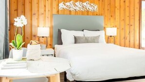 Une chambre d’hôtel avec un mur lambrissé en bois, un lit avec une literie blanche, une table de chevet avec une lampe et une petite plante en pot.