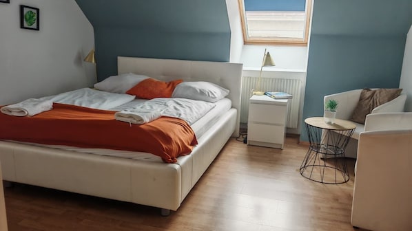 Un dormitorio con cama, mesita de noche, lámpara y una pequeña mesa redonda con una planta.