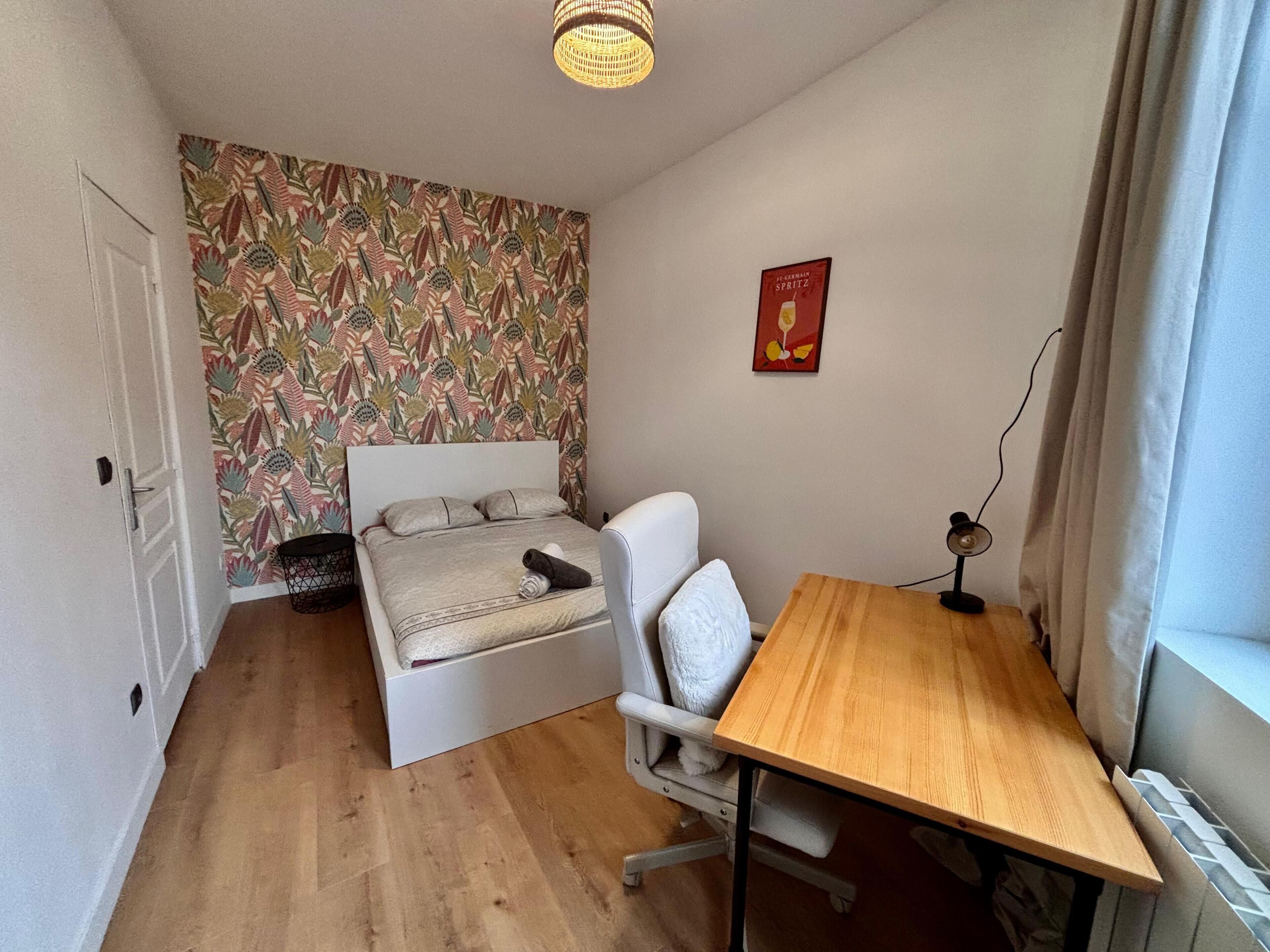 Een kleine, praktische kamer met een bed, een bureau en een stoel.