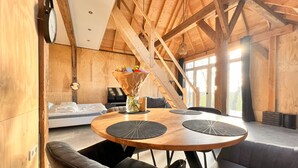 Een houten interieur met een ronde tafel, twee stoelen, een bank en een bed.