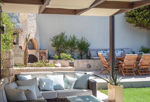 An outdoor patio with a stone wall, a wooden pergola, wicker furniture, and a variety of potted plants. - Caldera Blue Villa!! (Malevizi)