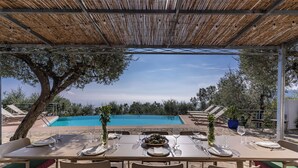 An outdoor dining area with a view of a swimming pool, surrounded by olive trees and lounge chairs. - Villa Chez Piè: Panoramic Views, Pool & Concierge (Massa Lubrense)