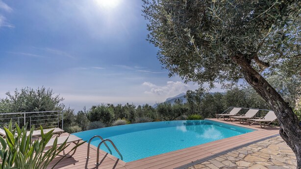 A swimming pool with a wooden deck, lounge chairs, and a metal railing. - Villa Chez Piè: Panoramic Views, Pool & Concierge (Massa Lubrense)