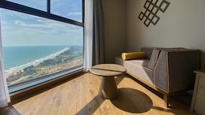 Une chambre moderne dotée d’une grande fenêtre donnant sur la côte, d’un canapé avec un coussin et d’une petite table ronde.