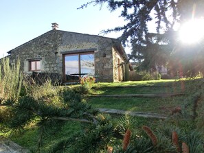 Una casa de piedra con un amplio ventanal corredera, una ventana pequeña y una terraza de madera.