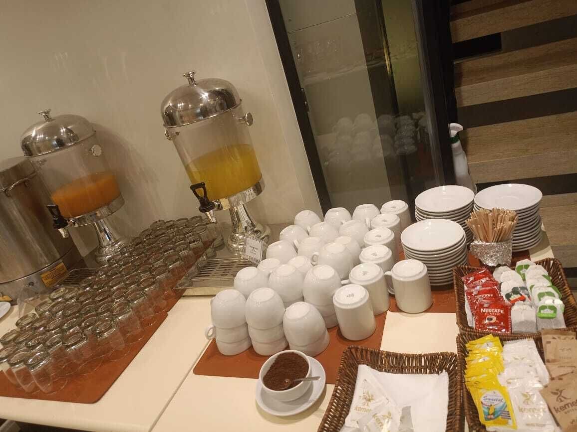 A buffet setup with multiple serving stations, including a coffee dispenser, a variety of bowls and plates, and a selection of packaged foods.