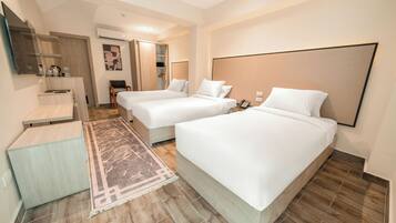 Quarto de hotel com duas camas, uma escrivaninha, uma cadeira, um espelho e um guarda-roupa.