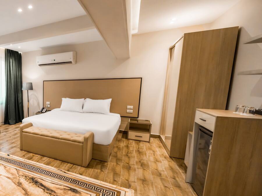A modern hotel room with a large bed, a bedside table, a desk, and a built-in oven.