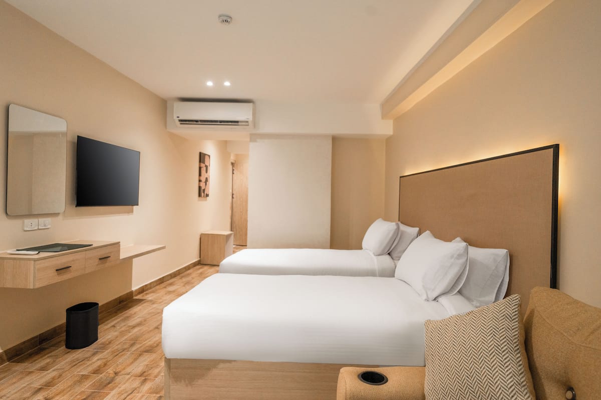 A modern hotel room with a large bed, a bedside table, a TV, and an air conditioning unit.