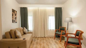 A hotel room with a beige sofa, two green chairs, a lamp, and a painting on the wall.