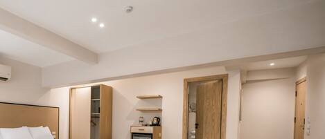 A modern hotel room with a bed, a small kitchenette, a wooden wardrobe, and a shower area.